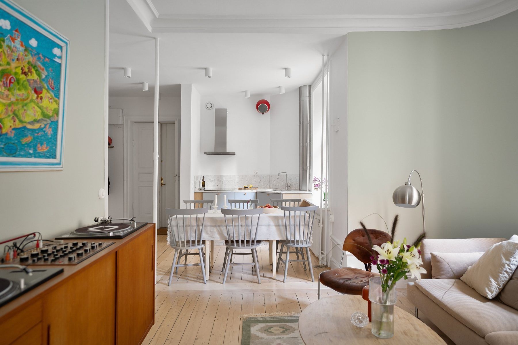 Séjour ouvert sur la cuisine : table et chaises en bois gris, parquet clair, fauteuil en cuir et canapé